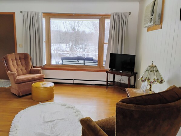A living room with a large window, a television, a lamp, and a chair.