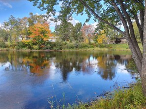 Un lac paisible où se reflètent les arbres, avec une maison visible au loin.