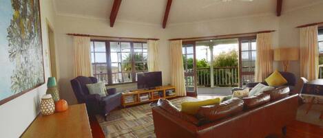 A spacious living room with a sofa, armchairs, a television, and a balcony with a view of greenery.