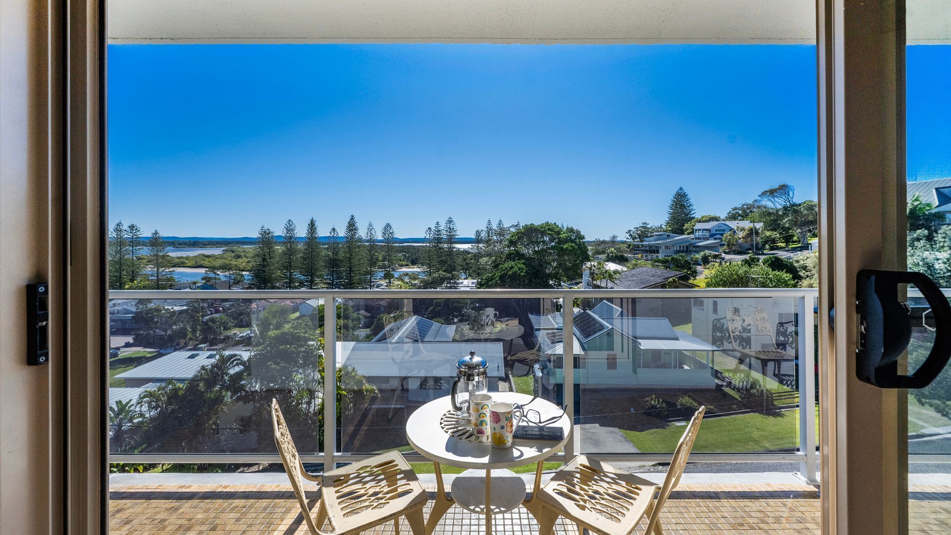 A balcony with a table and chairs, overlooking a residential area with houses and trees.