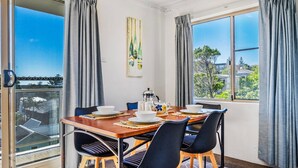 A dining area with a table set for four, chairs, a coffee pot, and a view of the outdoors. - Yamba Towers Unit 12 - Lifestyle Yamba (YAMBA)