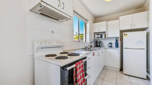 A compact kitchen with a stove, microwave, and refrigerator. - Yamba Towers Unit 12 - Lifestyle Yamba (YAMBA)