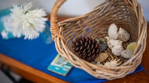 A wicker basket containing pine cones, seashells, and a white flower on a blue cloth. - Yamba Towers Unit 12 - Lifestyle Yamba (YAMBA)