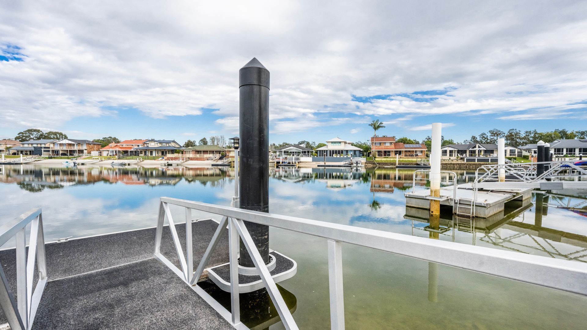 A marina with calm water, docked boats, and houses in the background.