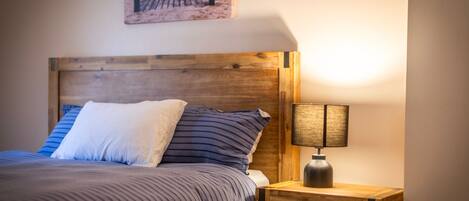A bed with a wooden headboard, a striped bedspread, and a pillow. There is a nightstand with a lamp beside the bed.