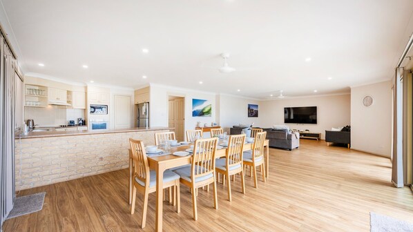 A modern apartment with a dining area, kitchen, living room, and a flat-screen TV. - A Mariners Cove - Lifestyle Yamba (YAMBA)