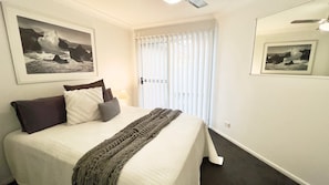 A bedroom with a bed, pillows, a blanket, and two framed photographs on the wall.