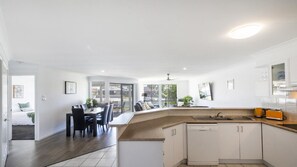 A modern kitchen with a dishwasher, a dining area with a table and chairs, and a view through large windows.