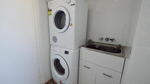 A compact laundry area with a washing machine and a sink. - Suncrest 4 - Lifestyle Yamba (YAMBA)