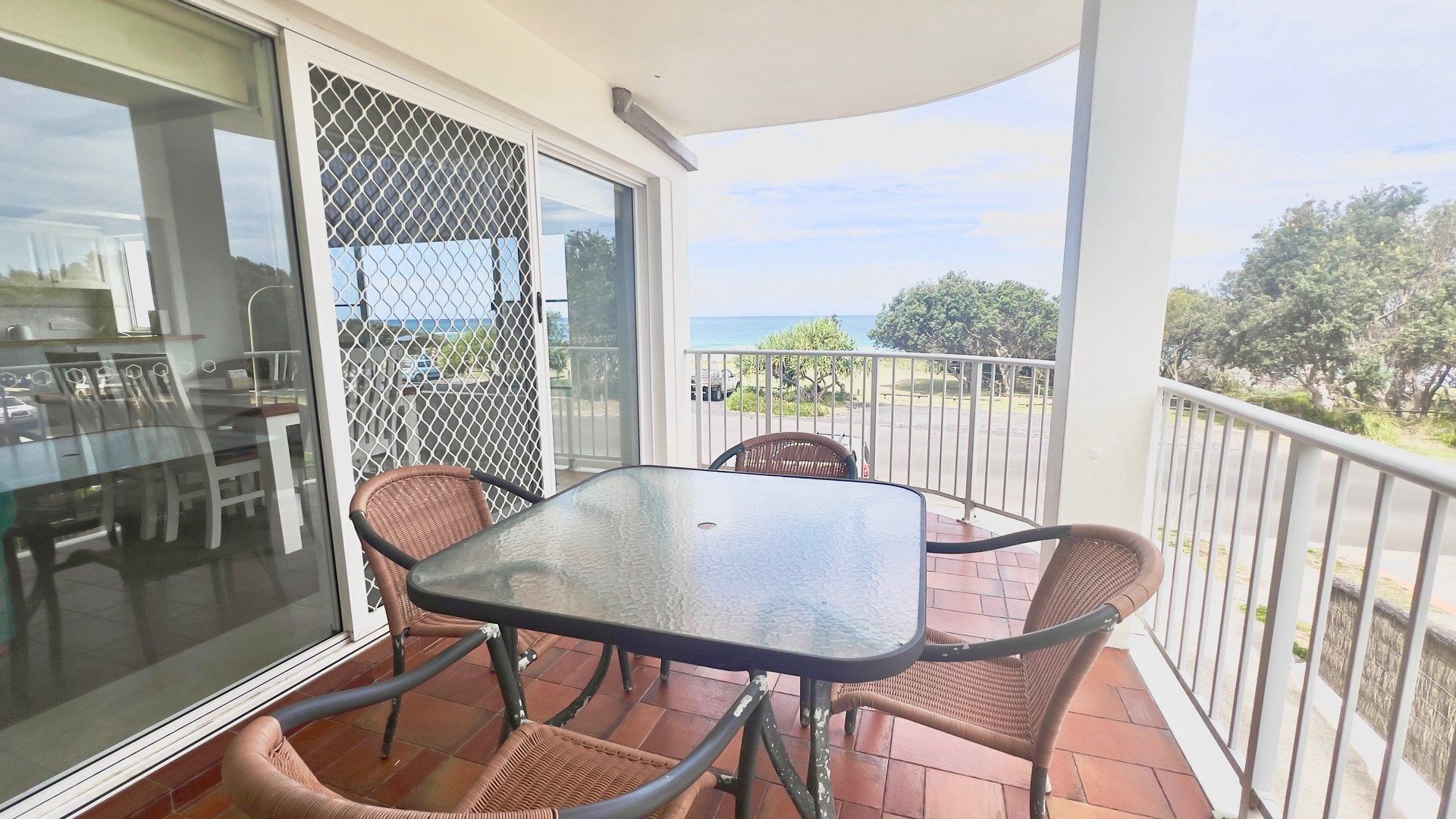 Un balcon avec une table en verre et des chaises en osier, donnant sur une zone côtière.