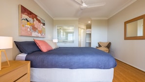 Une chambre à coucher avec un grand lit, un ventilateur de plafond, un tableau, une chaise et un miroir.