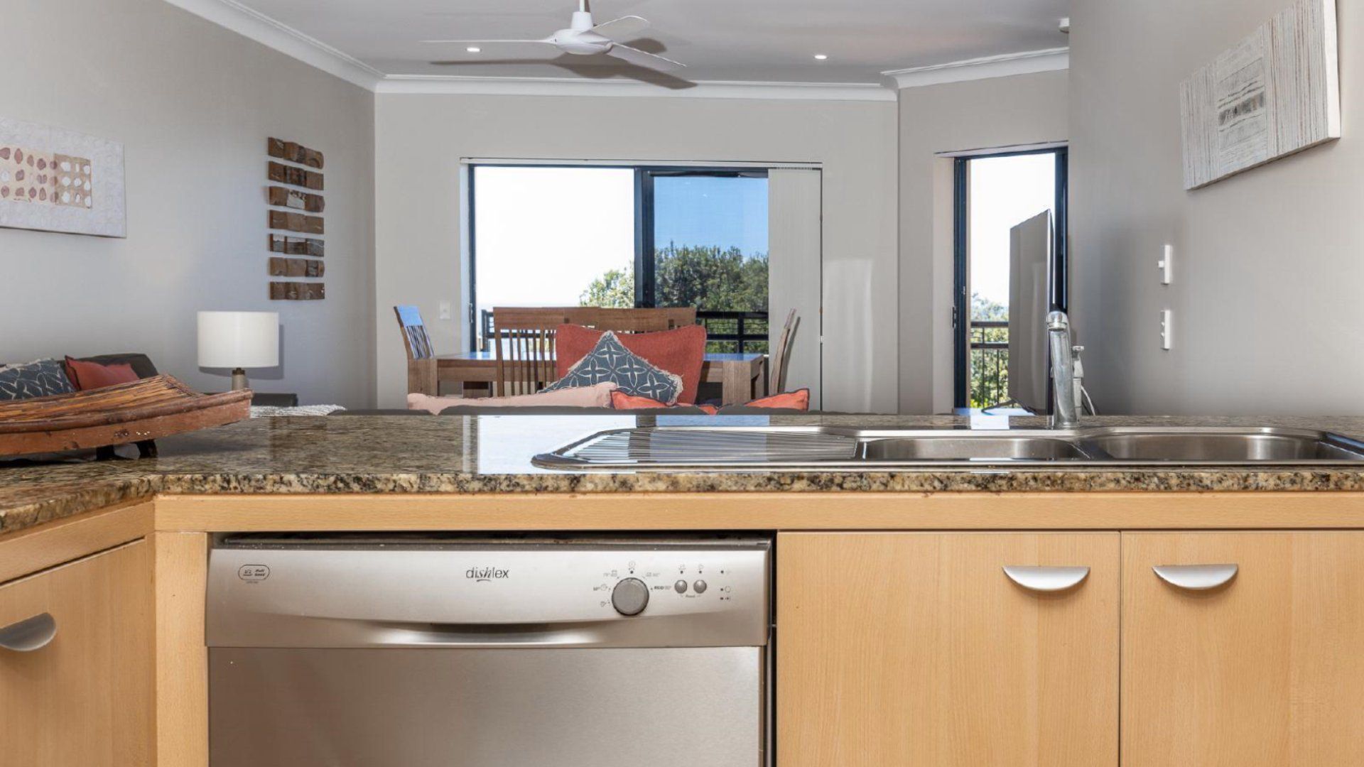 A modern kitchen with a dishwasher, a dining area with a table and chairs, and a view of the outdoors.