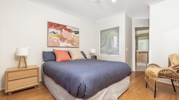 A bedroom with a bed, bedside tables, a chair, a window, and a painting on the wall.