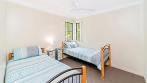 A bedroom with two single beds, a nightstand, a lamp, and a ceiling fan.