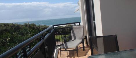 A balcony with a view of the ocean, a chair, and a table.