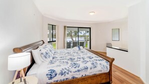 Relax in this serene bedroom with a large bed, a bedside table, and a window offering a view of the outdoors.