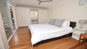 Un dormitorio con cama, mesita de noche, una silla, ventilador de techo y un armario corredero.