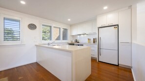 A modern kitchen with white cabinetry, a stainless steel refrigerator, and a built-in island with a sink. - Lighthouse Unit 2 - Lifestyle Yamba (YAMBA)