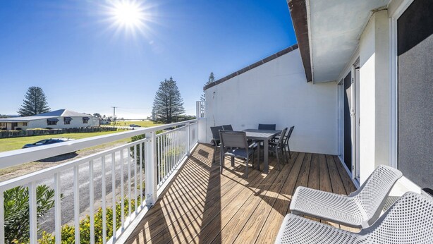 Una terraza de madera con mobiliario exterior y baranda blanca, con vistas a un césped.