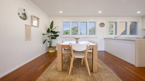 Un comedor con una mesa redonda, sillas, una planta en maceta y vistas al exterior a través de ventanas.
