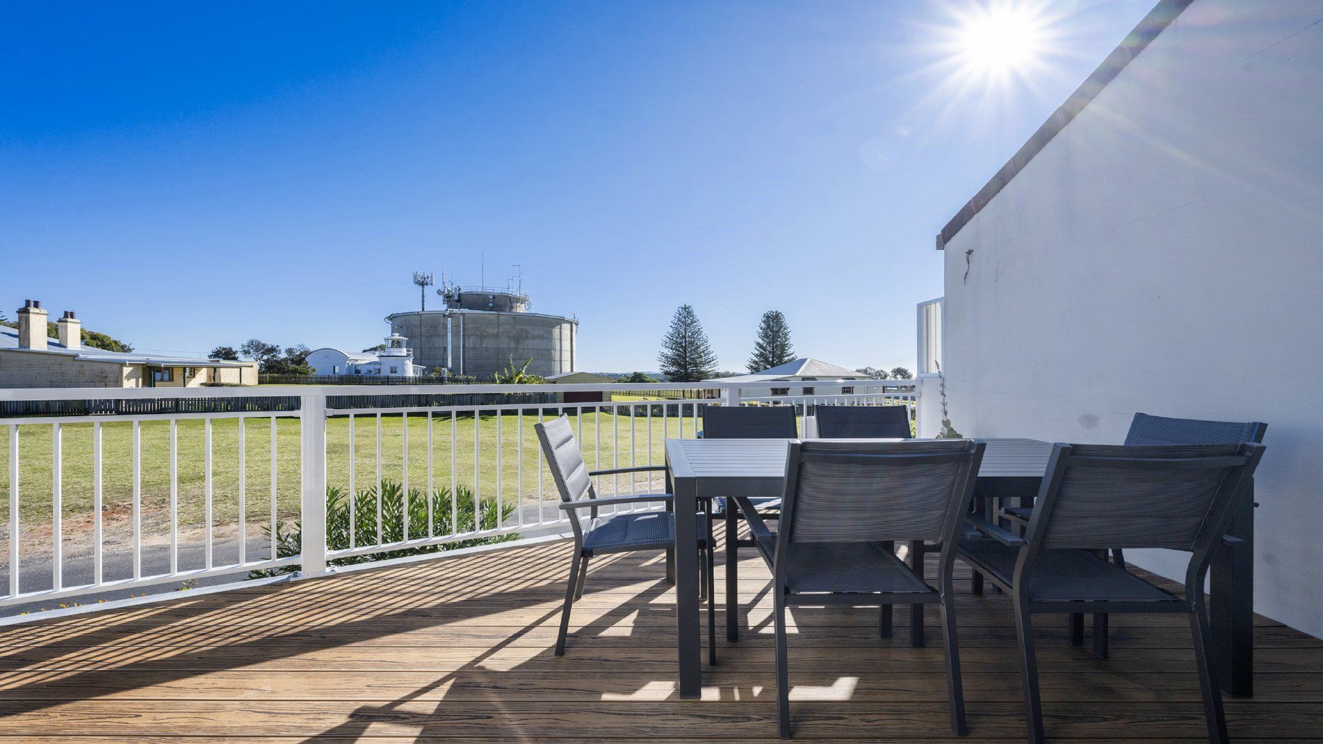 Una terraza con mobiliario exterior, una cerca blanca y vista a un silo y edificios al fondo.