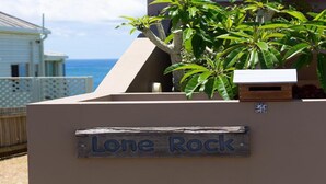 Skilt med teksten 'Lone Rock' på en bygnings facade med udsigt til havet i baggrunden.