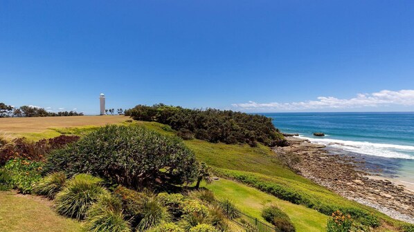 A coastal landscape with a lighthouse, grassy areas, and a rocky shoreline.