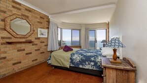 Et hotelværelse med en murstensvæg, et stort vindue med havudsigt, en seng med et blomstret sengetæppe og et trænatbord med en lampe.