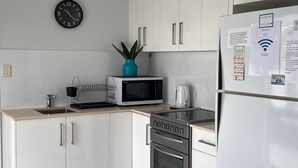 Une cuisine moderne avec des meubles blancs, un four à micro-ondes, une bouilloire et un réfrigérateur.