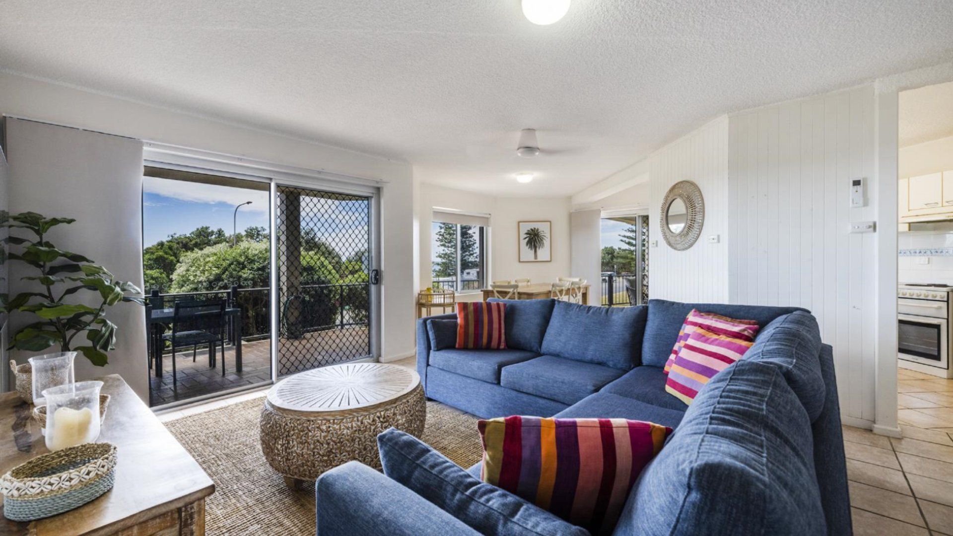 A living room with a blue sofa, a round woven coffee table, and a view through a sliding glass door to an outdoor area.