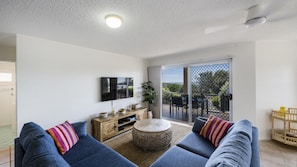 Relax in this stylish living room with a flat-screen TV, comfortable sofas, and a sliding door leading to an outdoor area with a beautiful view.