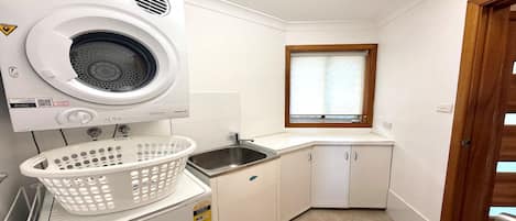 A compact laundry room with a washing machine, a sink, and a window.