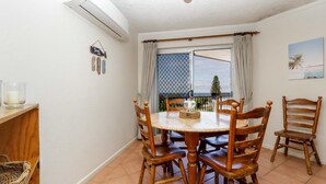Uma área de refeições com uma mesa redonda e cadeiras de madeira, uma janela com vista e um ar condicionado fixado na parede.