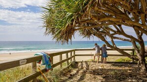 Uma praia com uma cerca de madeira, uma palmeira e um aviso de área sensível.