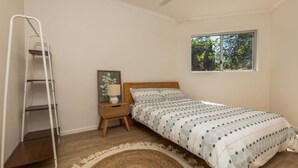 Um quarto com cama, mesa de cabeceira, abajur, escada, janela e tapete.