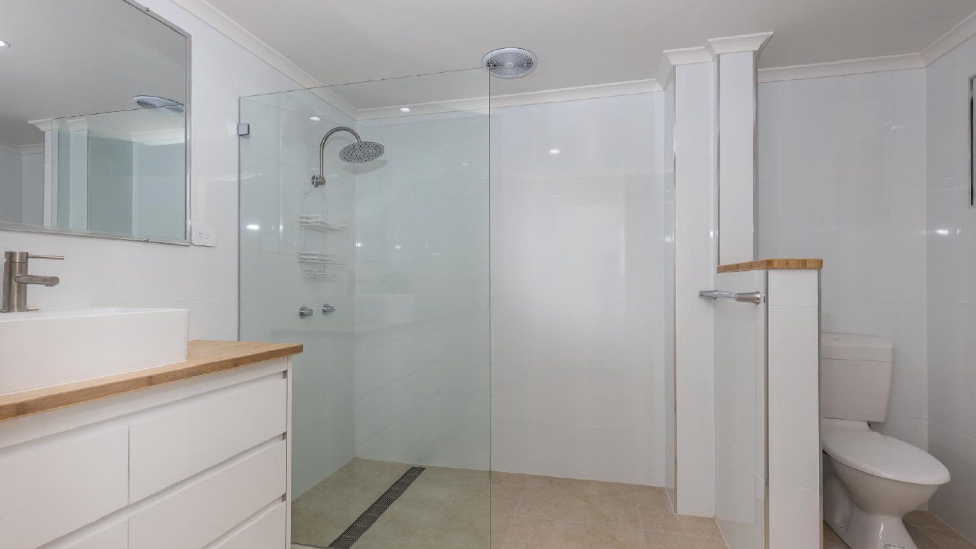 A modern bathroom with a glass-enclosed shower, a white toilet, and a vanity with a wooden countertop.