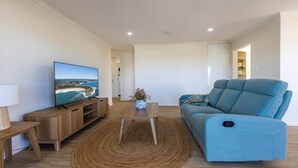 Uma sala de estar moderna com uma televisão de tela plana, um sofá azul, uma mesa de centro de madeira e um tapete tecido.