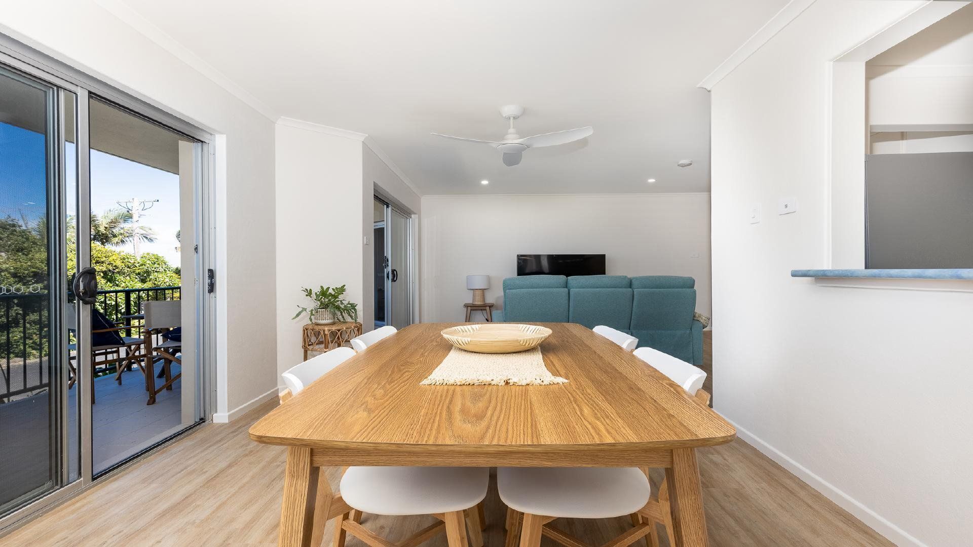 Een eetgedeelte met een houten tafel en stoelen, een plafondventilator en een uitzicht door een glazen deur op een terras.