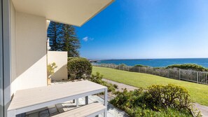 A balcony with a view of the ocean, a grassy lawn, and a wooden fence.