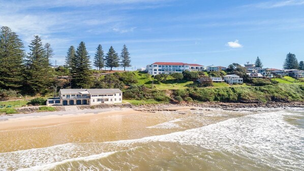 A coastal hotel with multiple buildings, a beach, and a forested hillside.