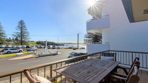 Een balkon met een tafel en stoelen, uitkijkend op een parkeerplaats met auto’s en een uitzicht op zee.