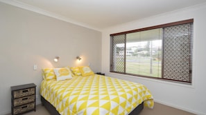 Cozy retreat with a bed featuring a geometric patterned bedspread, a large window, and a nightstand with a woven basket.