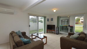 A living room with two sofas, a coffee table, a TV, and a sliding glass door leading to a balcony.