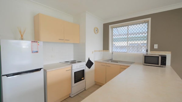 Kitchen area with a refrigerator, stove, and microwave, offering a view of the outside through the window.