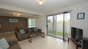 Relax in this stylish living room with a large sofa, flat-screen TV, and sliding glass door to a covered patio.
