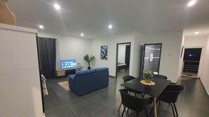 A modern living room with a blue sofa, a dining table with chairs, and a flat-screen TV on a stand. - Duzu Nature View Curacao (Tera Kora)