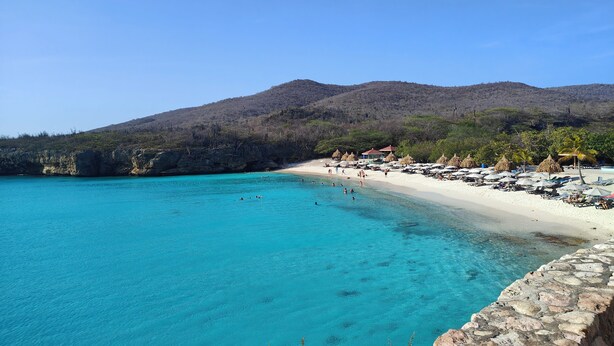 A beach with clear turquoise water, white sand, and thatched-roof huts. - Duzu Nature View Curacao (Tera Kora)