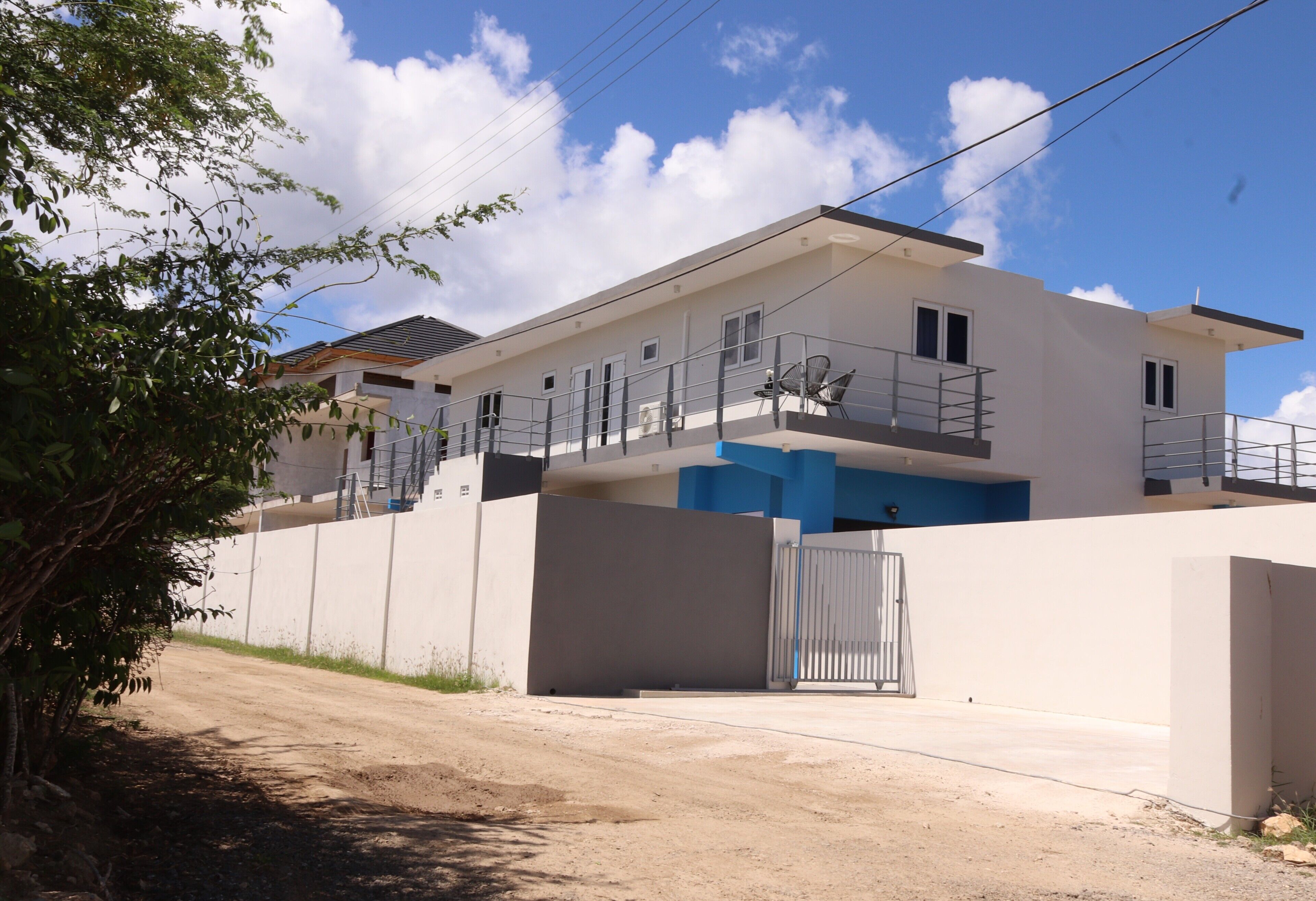 A modern two-story building with a gated entrance, a balcony, and a staircase leading to the upper floor.