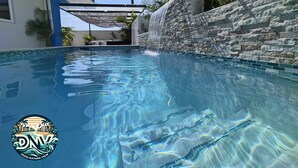 A clear swimming pool with a stone wall and a covered seating area. - Duzu Nature View Curacao (Tera Kora)