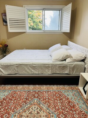 Relax in this serene bedroom with a comfortable bed positioned under a window with white shutters, set against a traditional patterned carpet.